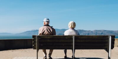 Two elderly people sitting on a bench looking at the mountains