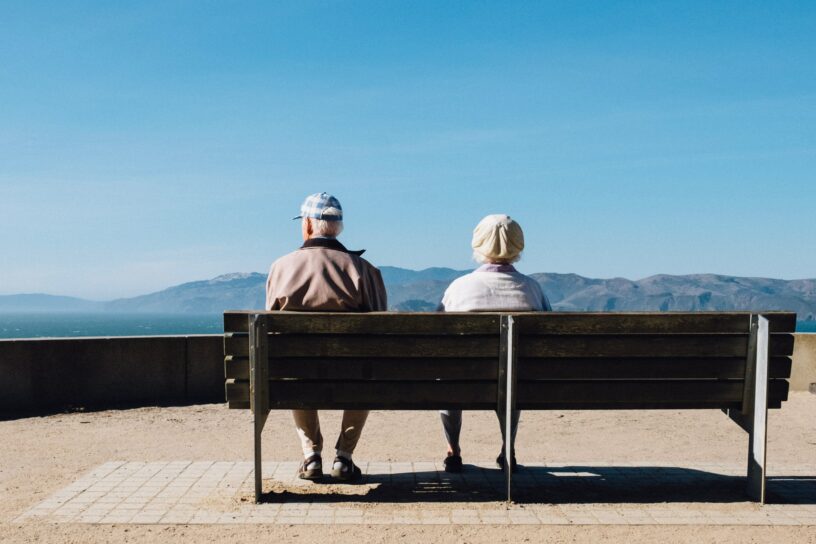 Two elderly people sitting on a bench looking at the mountains